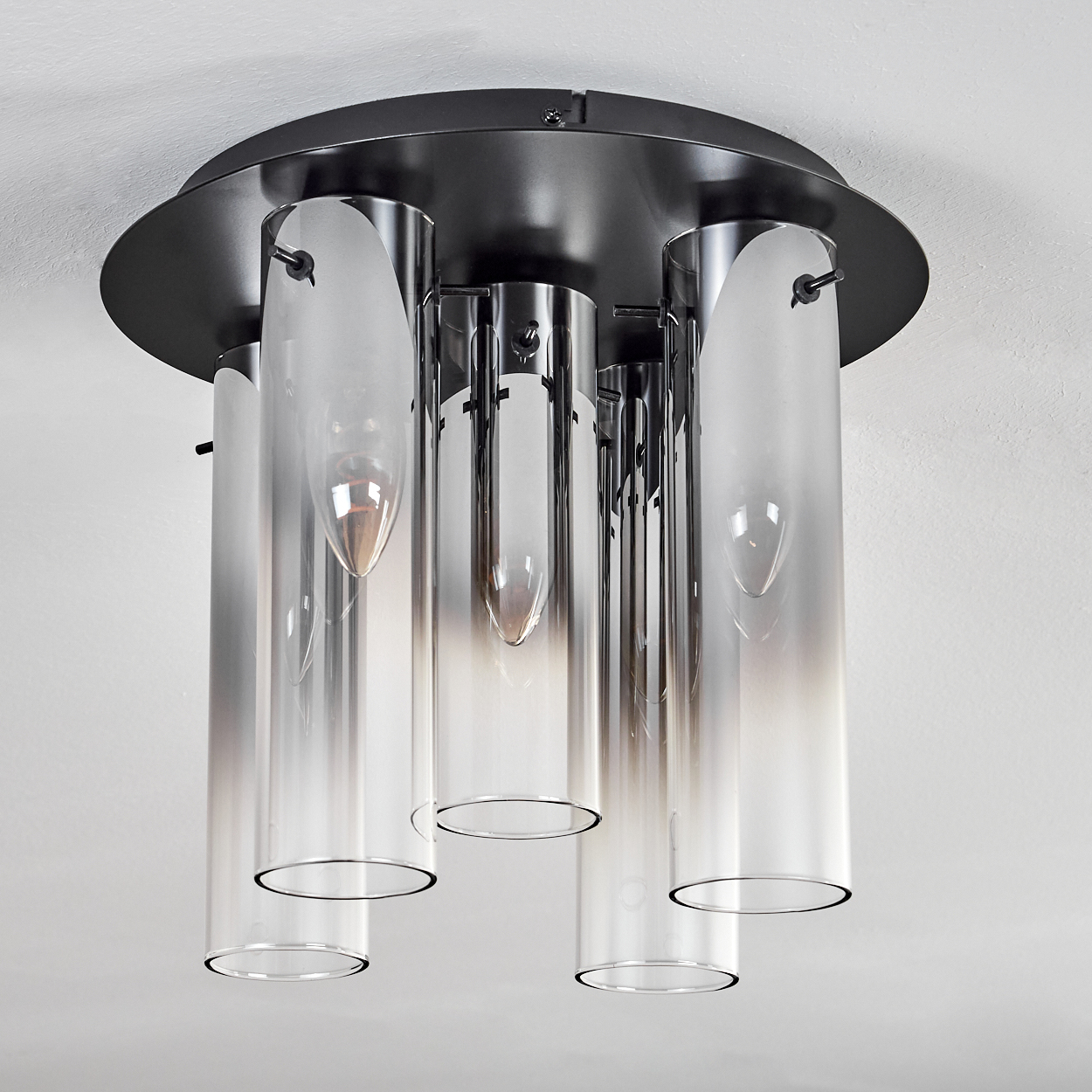 Deckenleuchte mit zylindrischen Glasschirmen und dunklem Metallsockel. Die Schirme sind farblich abgestuft, mit einem Hell-Dunkel-Übergang.