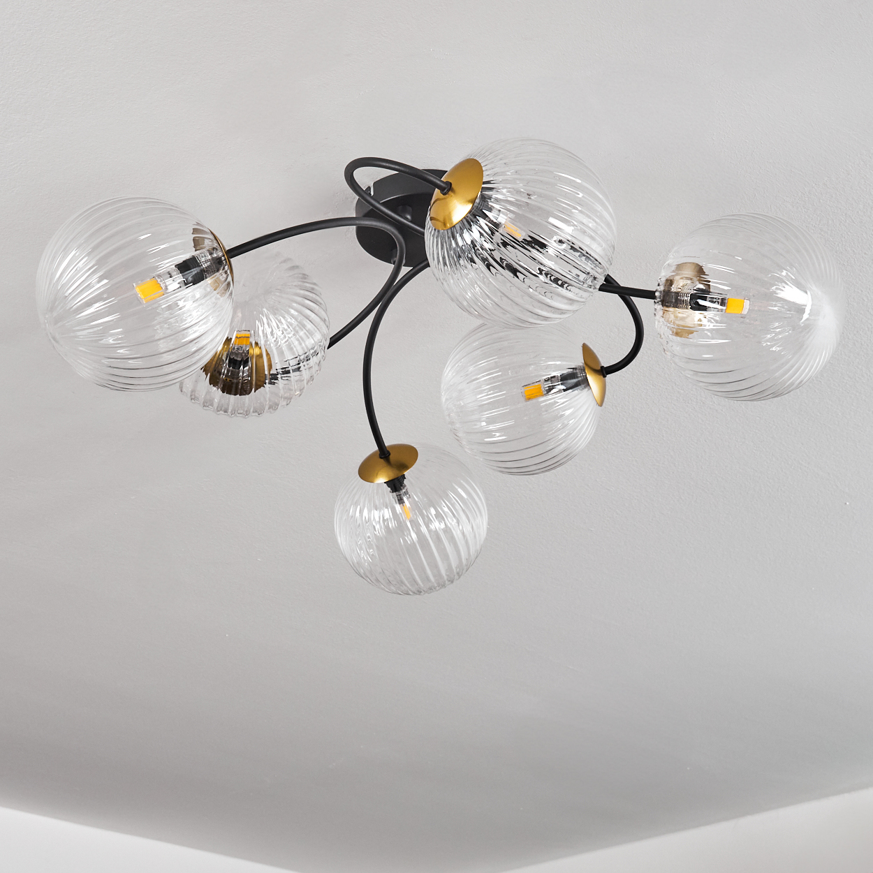 Moderne Deckenlampe mit sechs klaren, gerippten Glaskugeln, die an schwarzen, gebogenen Armen und goldenen Akzenten befestigt sind.