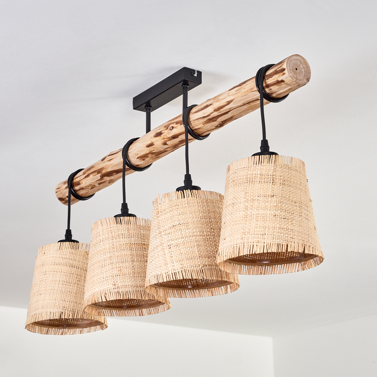 Eine Deckenlampe mit vier gewebten Lampenschirmen. Die Lampen hängen an einem Holzbalken. Die Leuchte hat einen schwarzen Metallsockel.