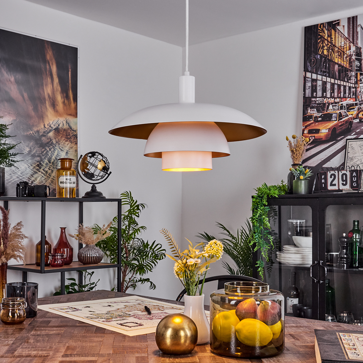 Ein modernes Zimmer mit weißer und goldener Lampe. Auf dem Tisch liegen Früchte und eine Karte. Regale halten Dekor. Kunstwerk an der Wand.
