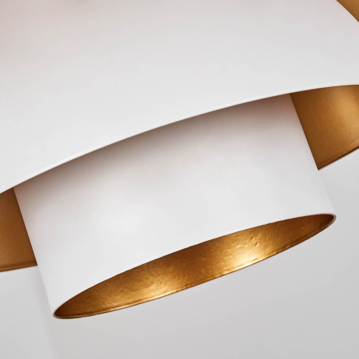 Nahaufnahme einer weißen und goldenen Lampe. Die Lampe hat Schichten aus Weiß und Gold. Der Hintergrund ist schlicht weiß.
