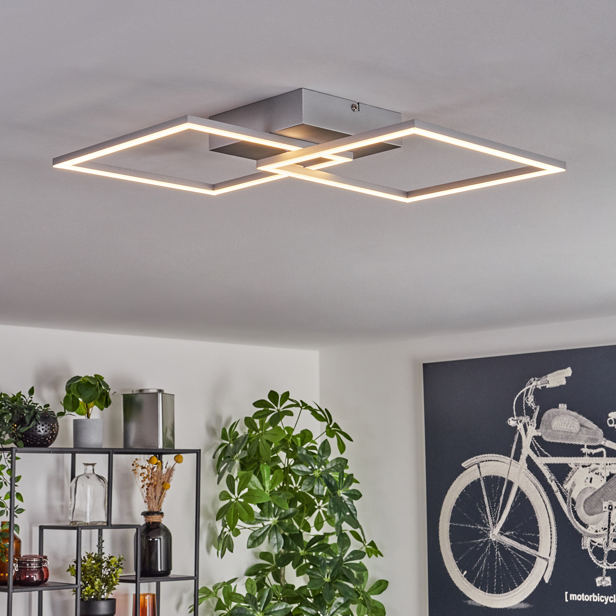 Moderne Deckenleuchte mit sich kreuzenden quadratischen Rahmen. Darunter ein Regal mit Pflanzen und ein Motorrad-Kunstwerk an der Wand.