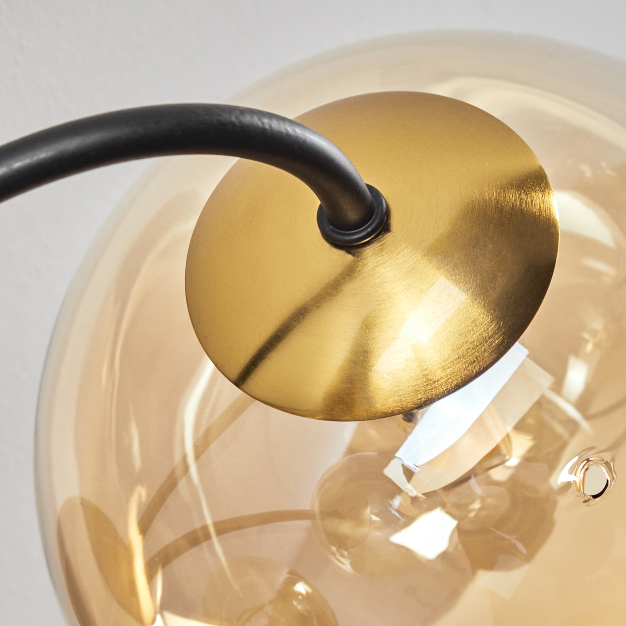 Nahaufnahme einer modernen Lampe. Sie hat eine goldene Scheibe, einen schwarzen gebogenen Arm und eine transparente bernsteinfarbene Glaskugel.
