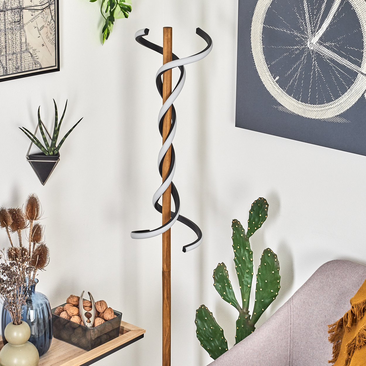 Ein stilvoller hölzerner Kleiderständer mit einem schwarz-weißen Spiraldesign steht vor einer weißen Wand. Pflanzen und Dekoration umgeben ihn.