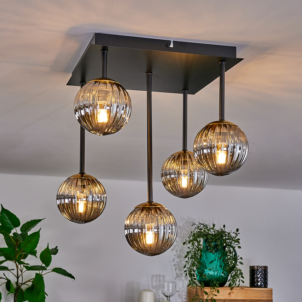 Eine moderne Deckenlampe mit fünf kugelförmigen Lampenschirmen. Die Schirme sind klar mit einem Braunstich, das Licht scheint.