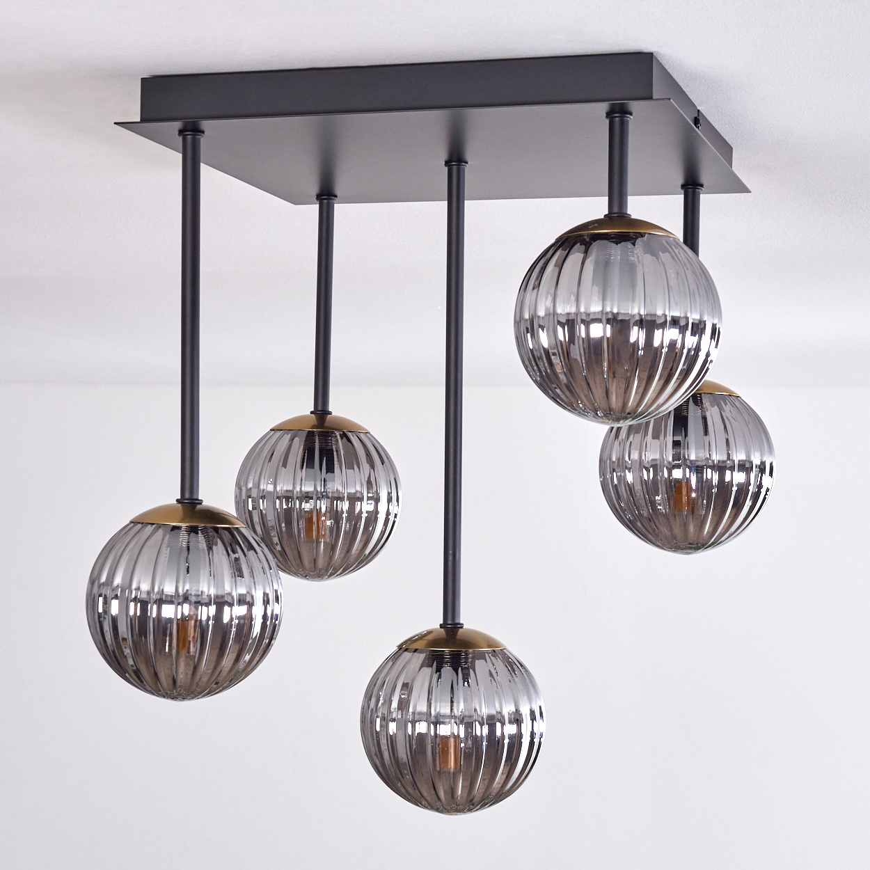 Ein moderner Kronleuchter mit fünf Glasschirmen. Die Schirme sind silber und gerippt, an einer schwarzen quadratischen Basis aufgehängt.