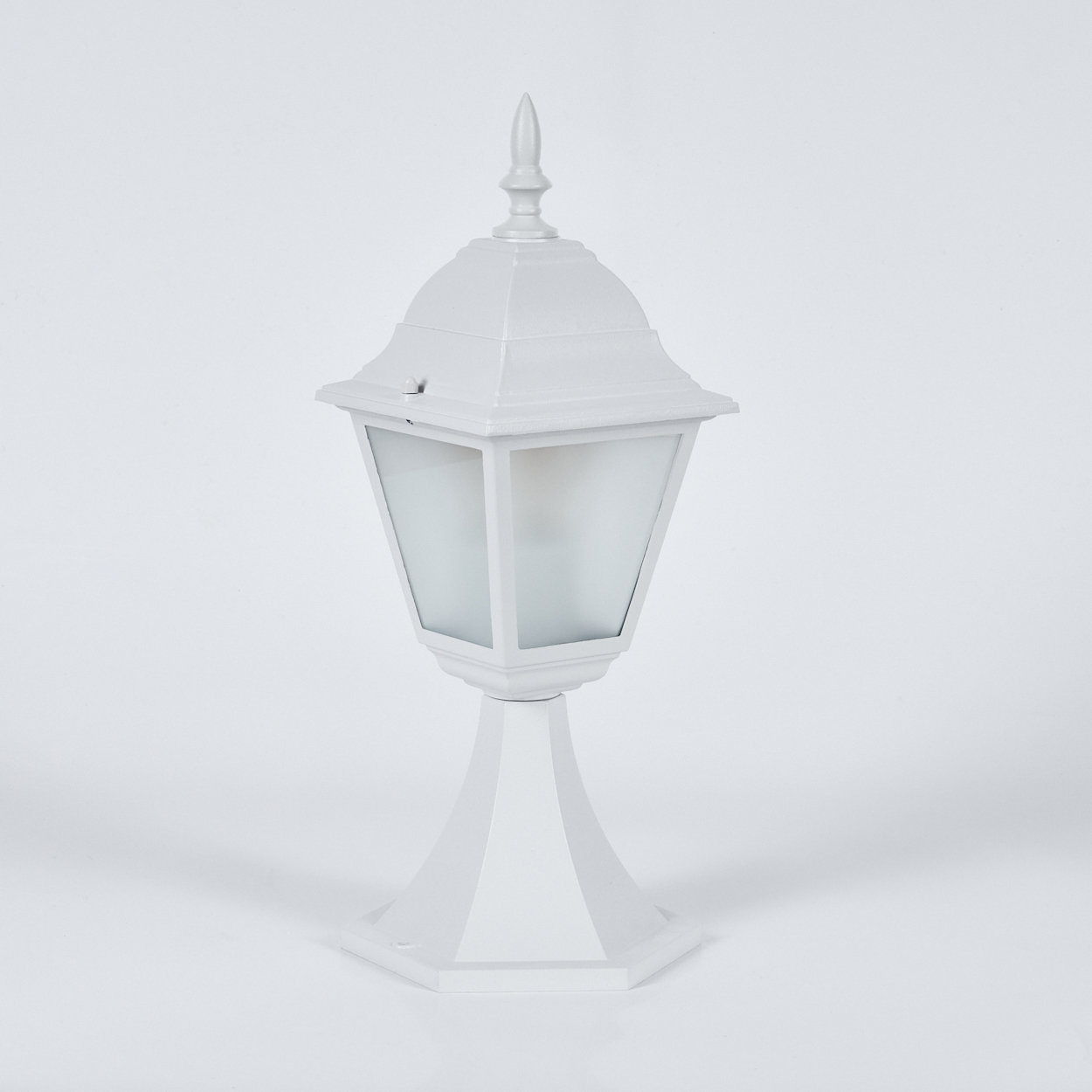 Eine weiße Außenlampe steht vor einem weißen Hintergrund. Die Lampe hat einen sechseckigen Sockel, einen konischen Schaft und einen Glaskerzenhalter.