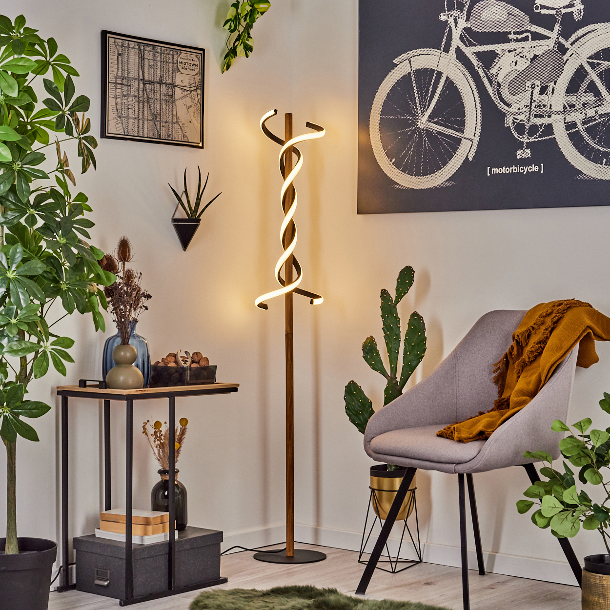 Ein modernes Wohnzimmer mit einer Spirallampe, einem grauen Stuhl mit gelbem Überwurf, Pflanzen und einem Motorrad-Kunstdruck an der Wand.