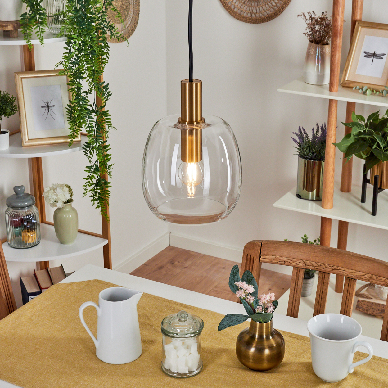 Ein Esszimmer mit einer Glashängelampe, einem Tisch mit gelbem Läufer, einem weißen Krug und Dekorationsartikeln auf Regalen.