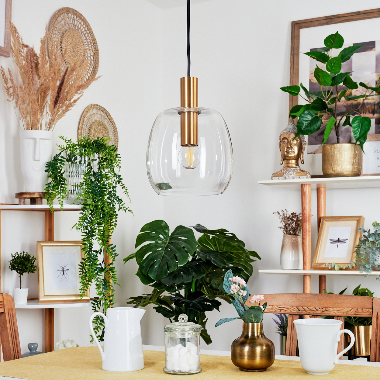 Ein Raum mit Pflanzen, einer Hängelampe, Regalen mit Dekorationen, einem Tisch mit Kanne, Glas, Tasse und Vase.