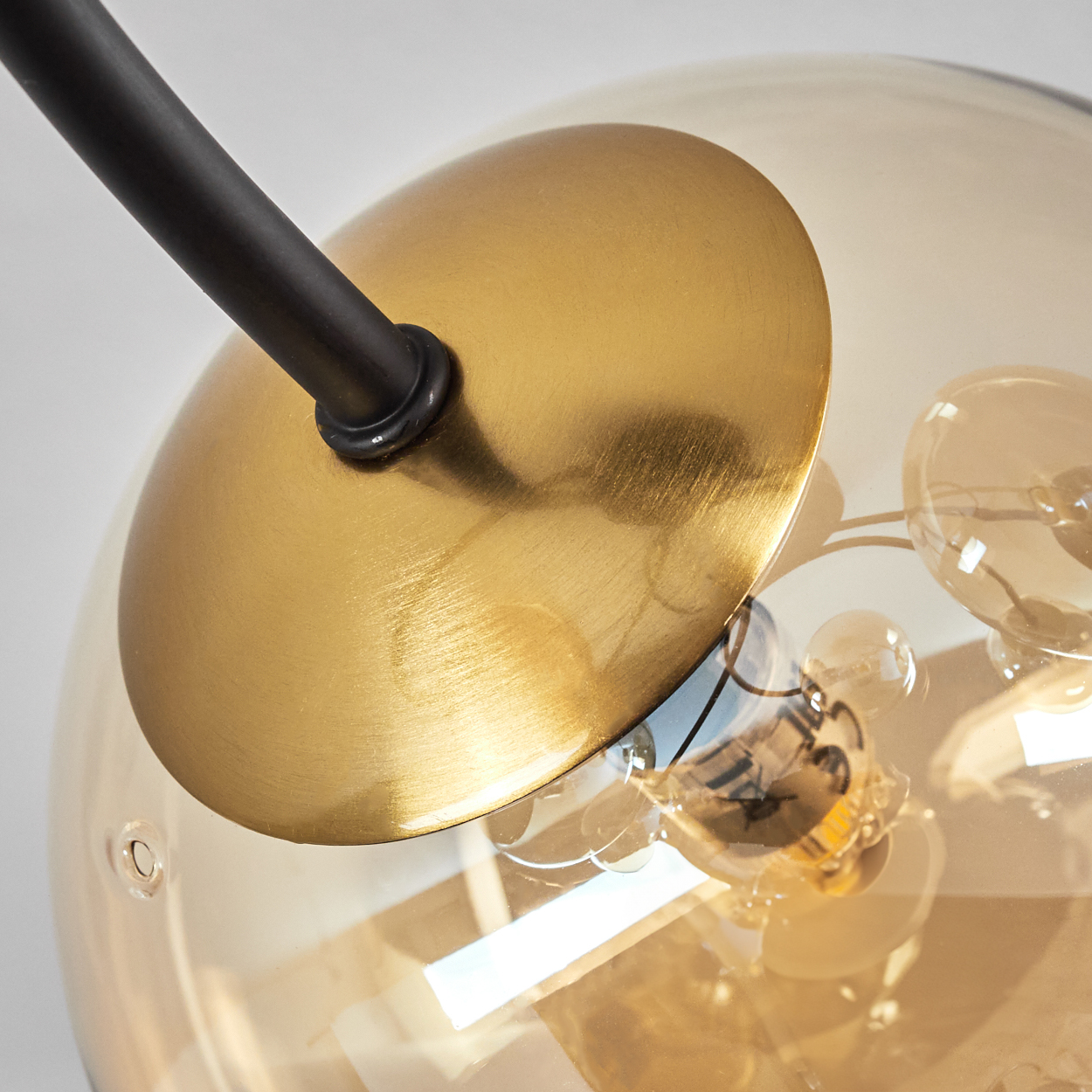 Nahaufnahme einer Lampe. Eine schwarze Stange ist an einer goldenen Scheibe befestigt. Eine klare Glaskugel hat kleine Glühbirnen im Inneren, vor weißem Hintergrund.