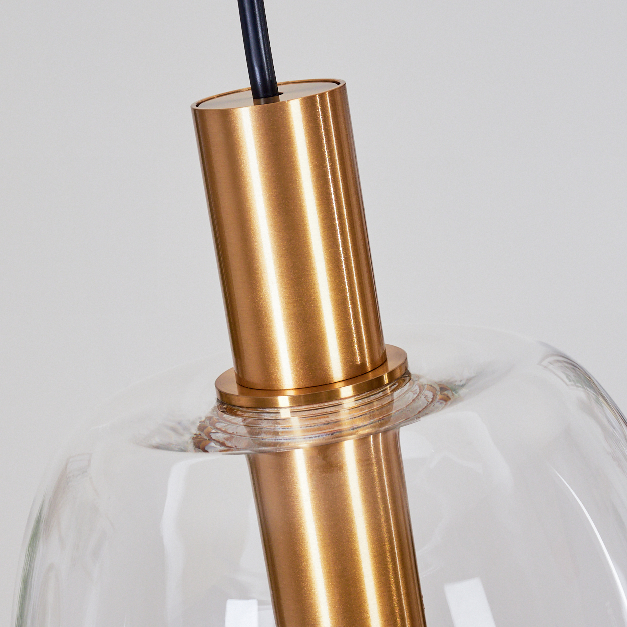 Nahaufnahme einer Glaslampe. Eine goldfarbene, zylindrische Metallstange geht durch einen klaren Glaskolben. Oben ein schwarzes Kabel.