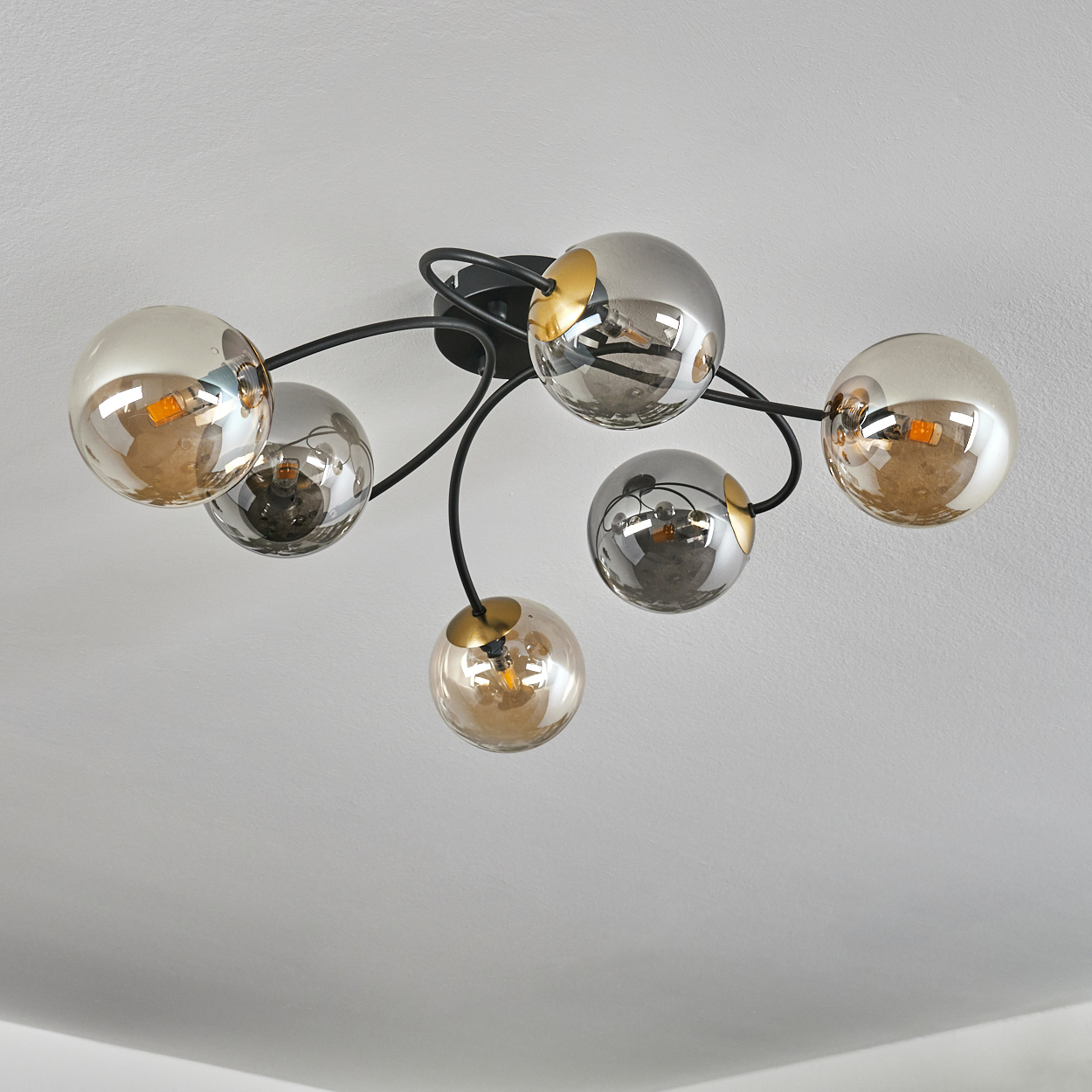 Deckenleuchte mit sechs kugelförmigen Glasschirmen, abwechselnd silber und gold, an schwarzen gebogenen Armen, vor weißer Decke.