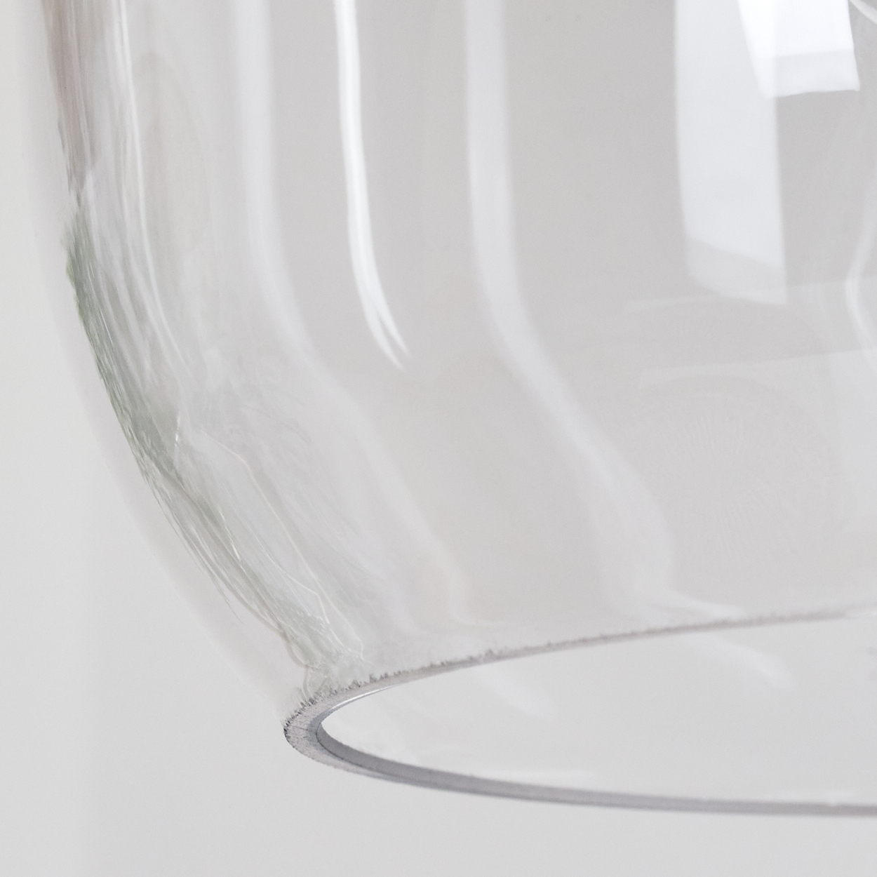 Nahaufnahme eines durchsichtigen Glasobjekts mit gebogenem Rand. Weiche Beleuchtung, weißer Hintergrund. Das Glas reflektiert Licht.