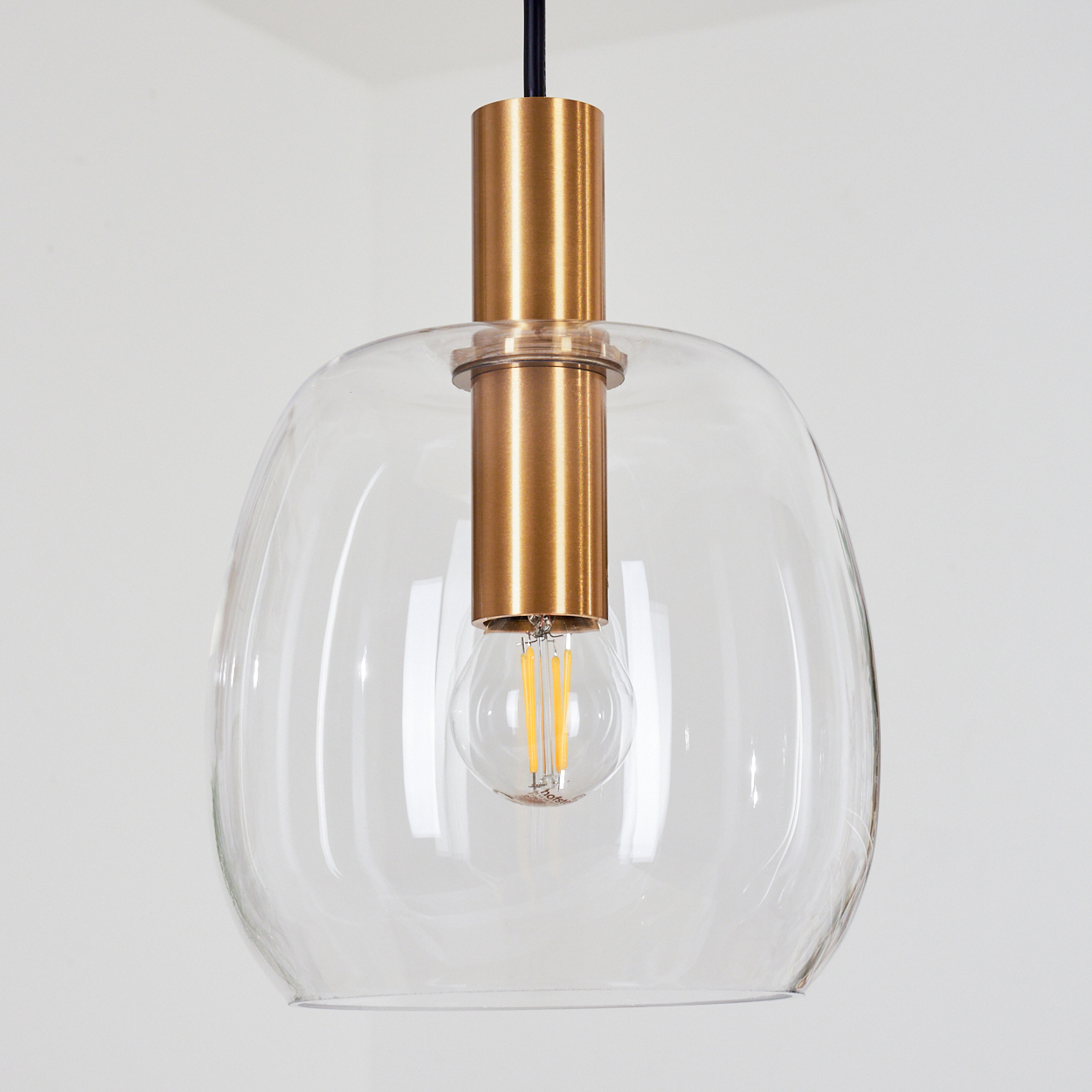 Eine transparente Glas-Hängeleuchte mit goldfarbenem Metallgestell und freiliegender Glühbirne, vor weißem Hintergrund.