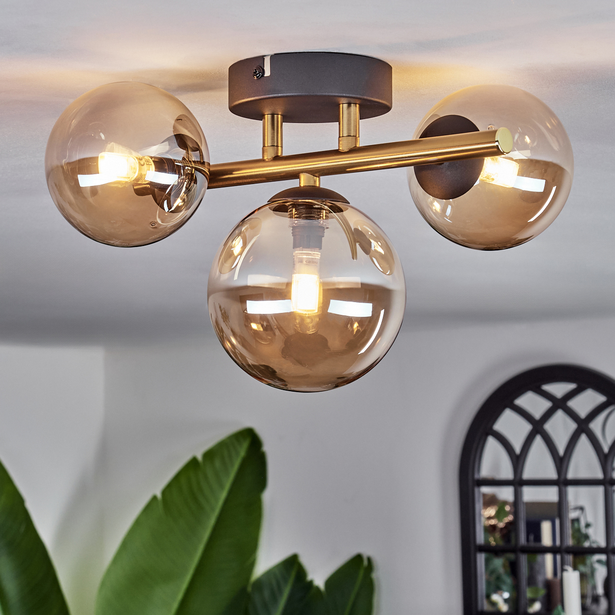 Deckenleuchte mit drei Glaskugeln. Die Leuchte ist bronze mit dunklem Graubasis. Licht von den Glühbirnen scheint durch.
