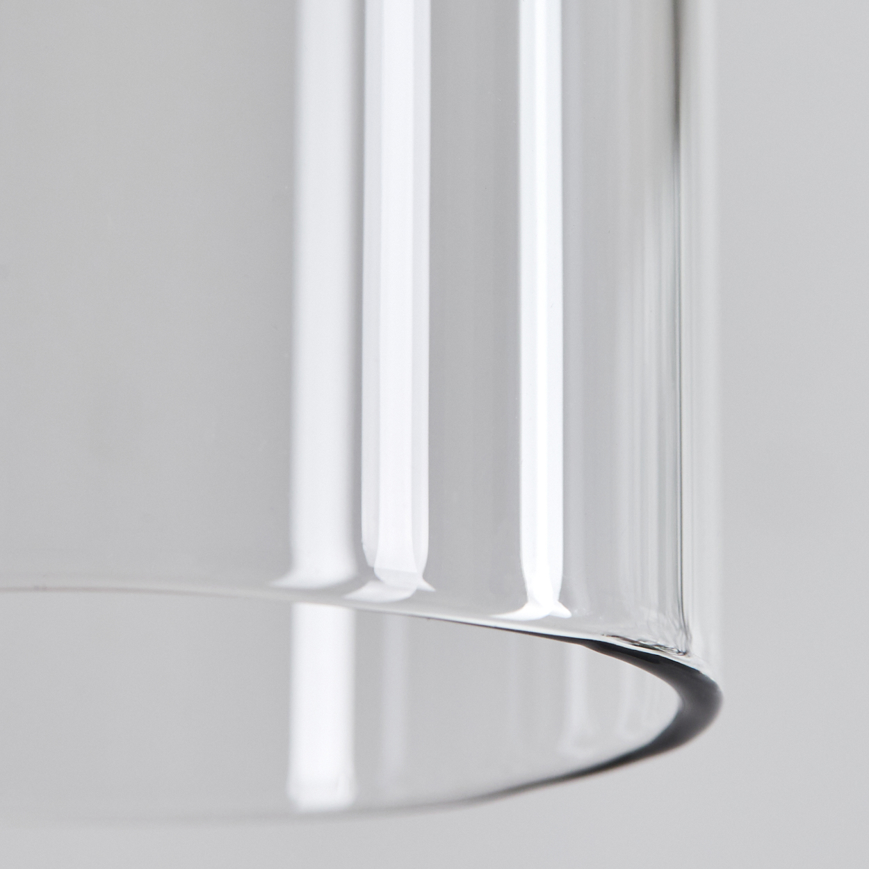 Nahaufnahme eines durchsichtigen Glaszylinders vor hellgrauem Hintergrund. Das Glas reflektiert Licht und hat abgerundete Kanten.
