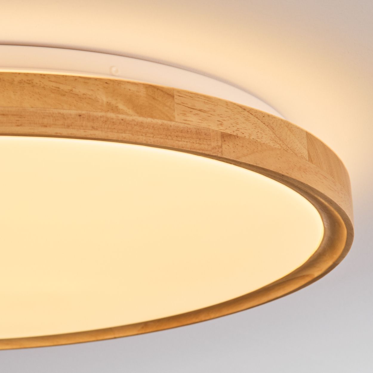 Nahaufnahme einer modernen Deckenleuchte. Es hat eine Holzverkleidung um ein helles, kreisförmiges Licht. Der Hintergrund ist weiß.
