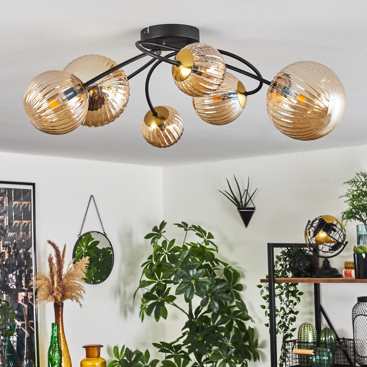 Deckenleuchte mit mehreren Kugelschirmen. Raum mit Pflanzen, Spiegel und Regalen mit Dekoration. Farben: Gold, Schwarz, Grün, Weiß.