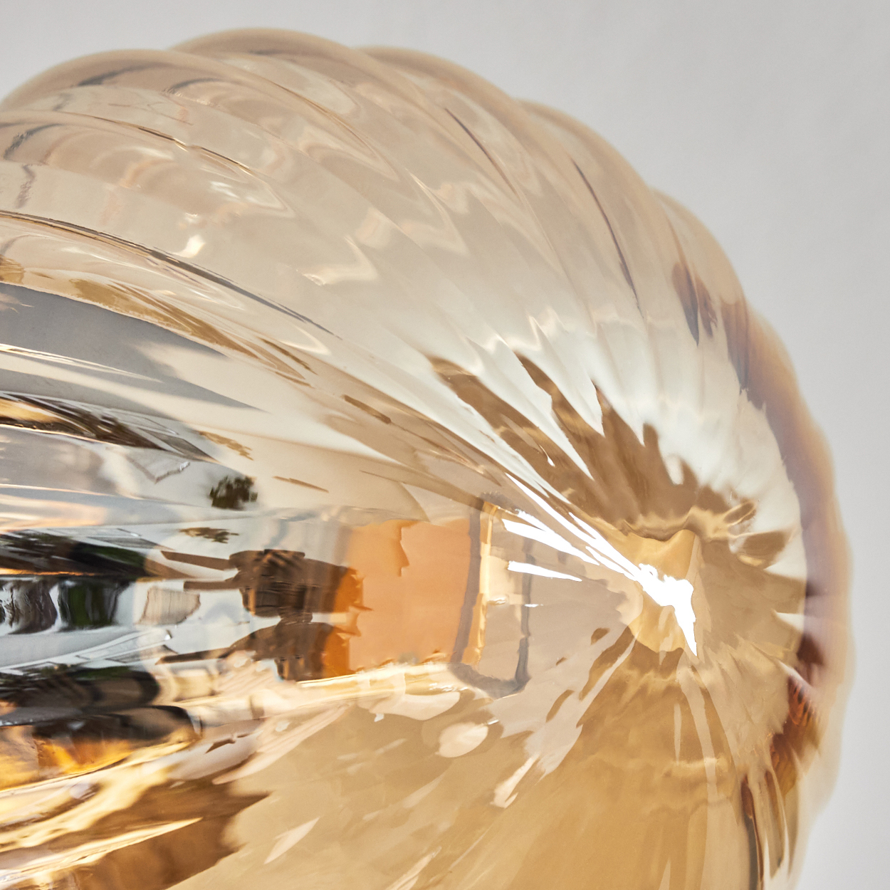 Nahaufnahme eines strukturierten, bernsteinfarbenen Glasobjekts. Das Glas hat ein geriffeltes Muster. Licht spiegelt sich auf der Oberfläche.