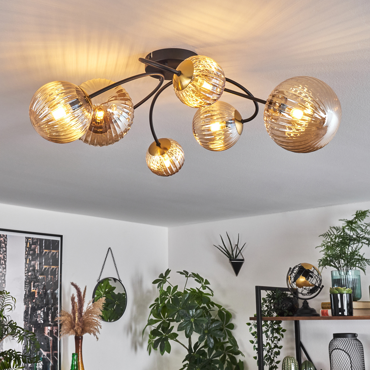 Eine Deckenleuchte mit sechs bernsteinfarbenen Glaskugeln. Der Hintergrund zeigt eine weiße Decke und ein Zimmer mit Pflanzen und Dekorationen.