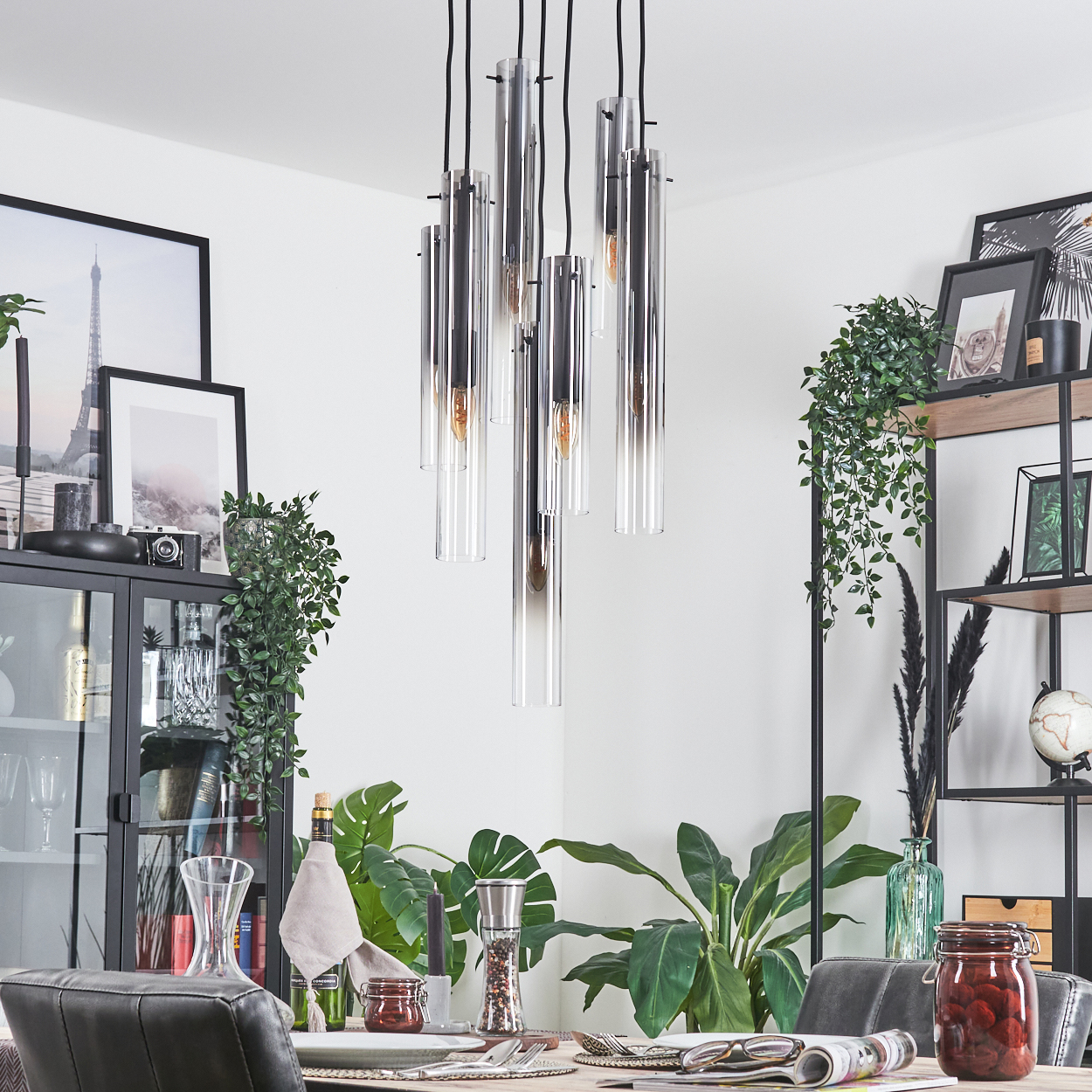 Ein Esszimmer mit modernem Kronleuchter, Tischdeko, Pflanzen und gerahmten Bildern. Ein Globus steht auf einem Regal.