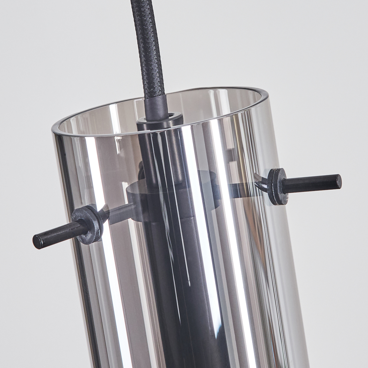Nahaufnahme einer modernen Leuchte. Sie hat einen zylindrischen Glasschirm, schwarze Metallkomponenten und ein schwarzes Kabel auf weißem Hintergrund.