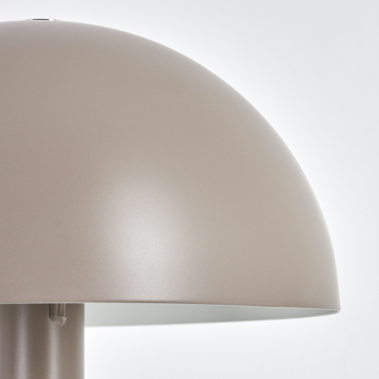 Eine beige pilzförmige Lampe vor weißem Hintergrund. Der Lampenschirm ist im Fokus, mit einem metallischen Sockel.