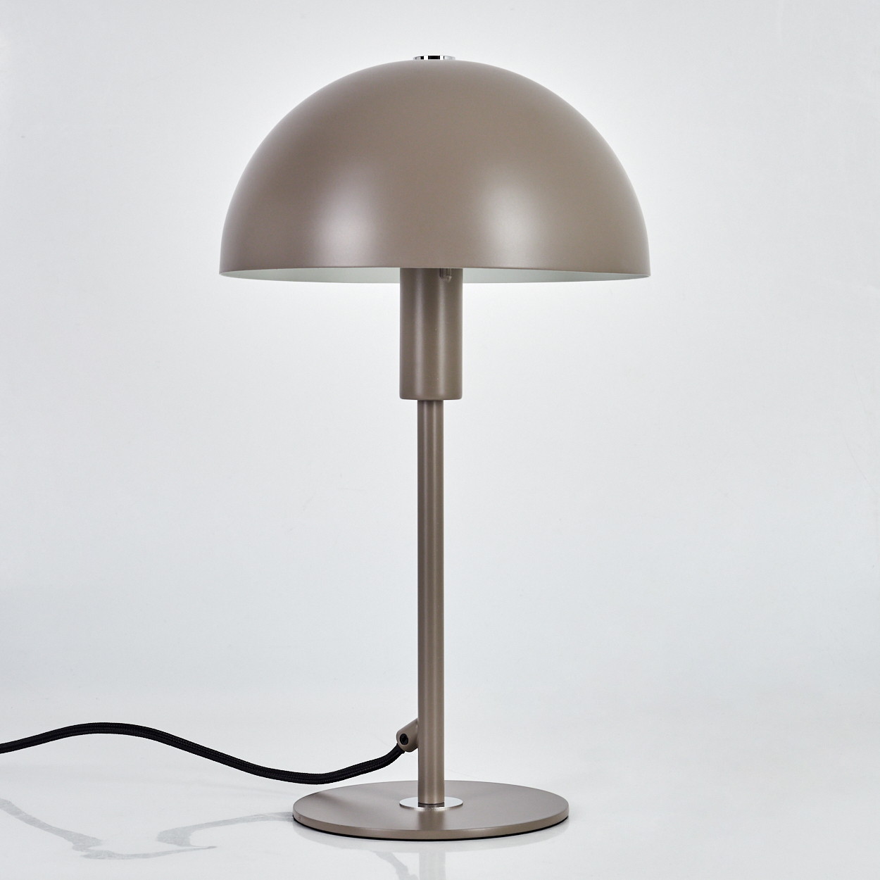Eine taupefarbene Tischlampe mit rundem Schirm und langem Stiel auf einem kreisförmigen Sockel. Ein schwarzes Kabel erstreckt sich nach links.