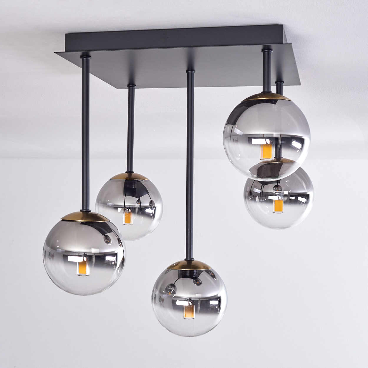 Moderne Deckenleuchte mit fünf Glasschirmen. Schwarze Metallstangen und eine quadratische Basis. Warmes gelbes Licht in den Kugeln.