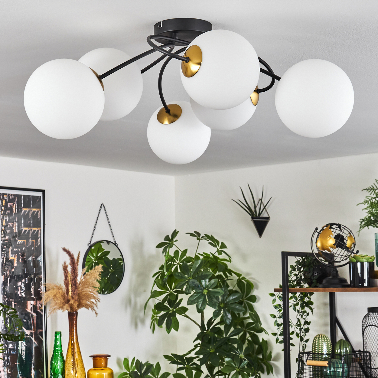 Deckenlampe mit weißen Kugeln und schwarzen Armen. Raumdekor umfasst Pflanzen, einen Spiegel und ein gerahmtes Bild. Pflanzen sind der Hauptfokus.