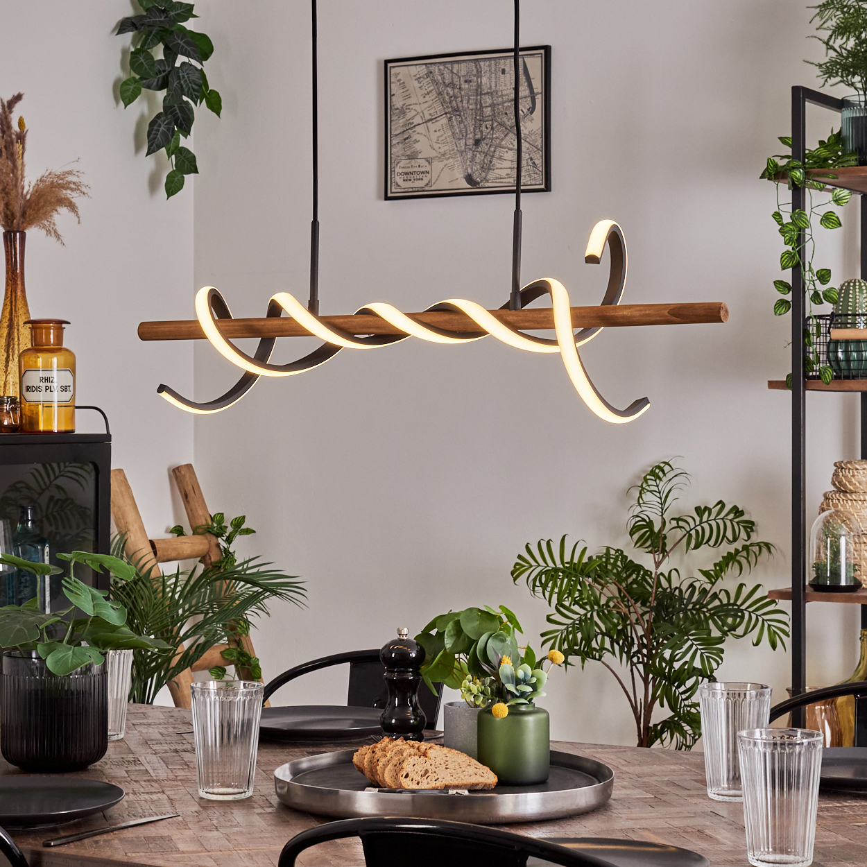 Esszimmer-Szene. Ein Holztisch ist mit Gläsern, Tellern und einem Serviertablett gedeckt. Über dem Tisch hängt eine moderne Leuchte.