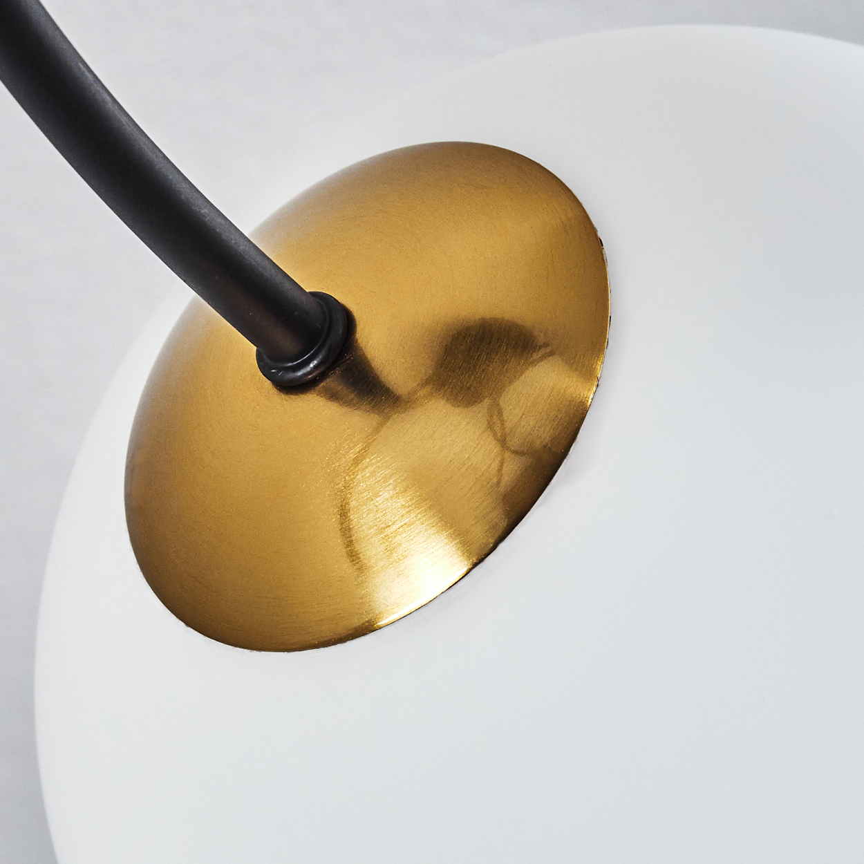 Nahaufnahme einer Lampe. Ein schwarzer Arm erstreckt sich von einer goldenen Scheibe, die mit einer weißen Kugel verbunden ist. Der Hintergrund ist verschwommen.