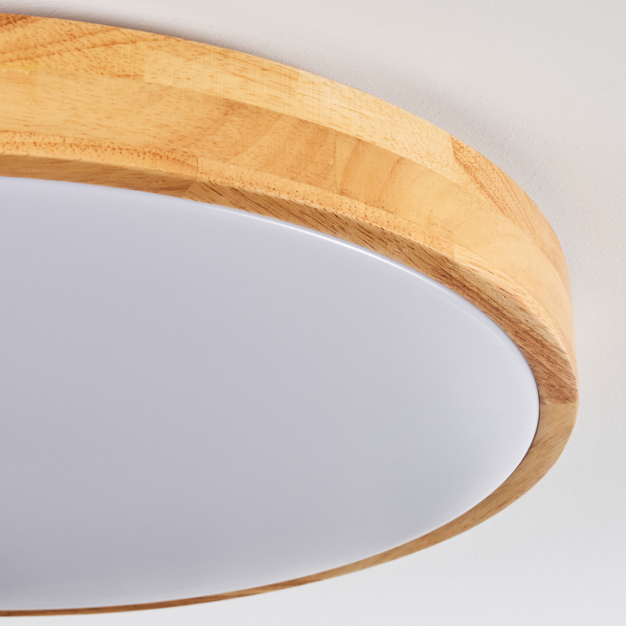 Nahaufnahme einer runden Deckenleuchte. Sie hat einen Holzrahmen und eine weiße, diffuse Lichtfläche.