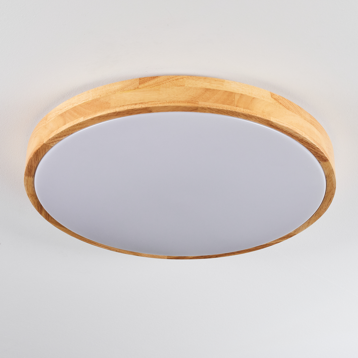 Eine runde Deckenleuchte mit Holzrahmen und weißer, mattierter Lichtabdeckung. Der Hintergrund ist eine schlichte weiße Decke.