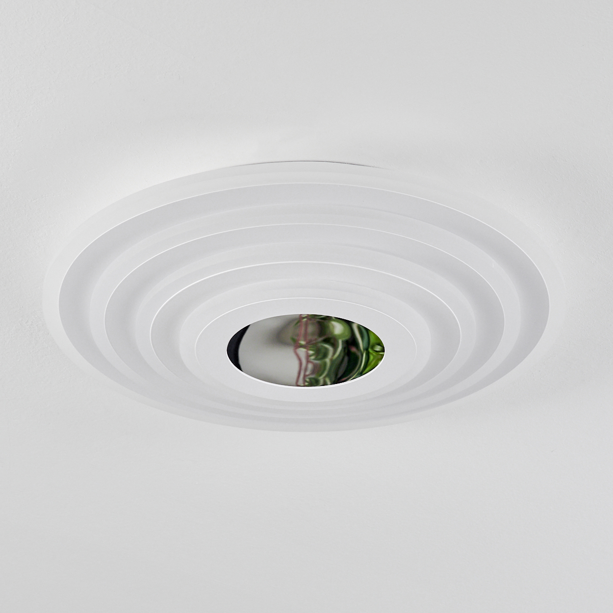 Weiße Deckenleuchte mit konzentrischen Ringen. Zentrum zeigt Grün. Bild von unten aufgenommen.