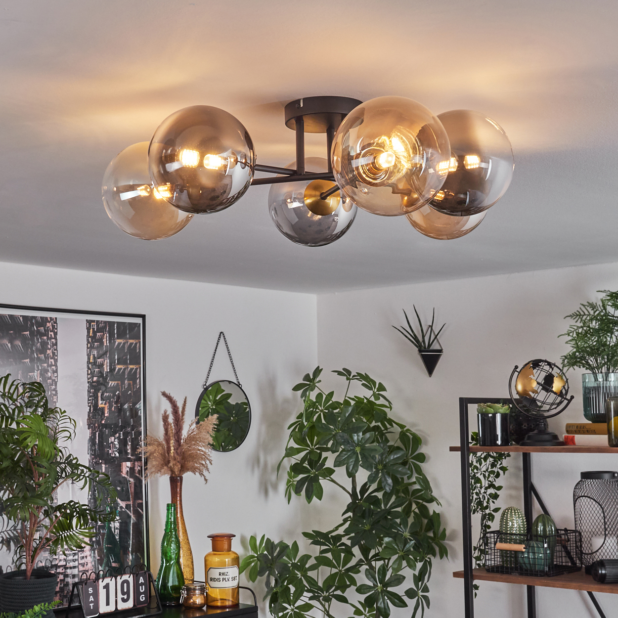 Eine moderne Deckenleuchte mit Glaskugeln beleuchtet einen Raum mit Pflanzen, einem Spiegel und einem gerahmten Bild.
