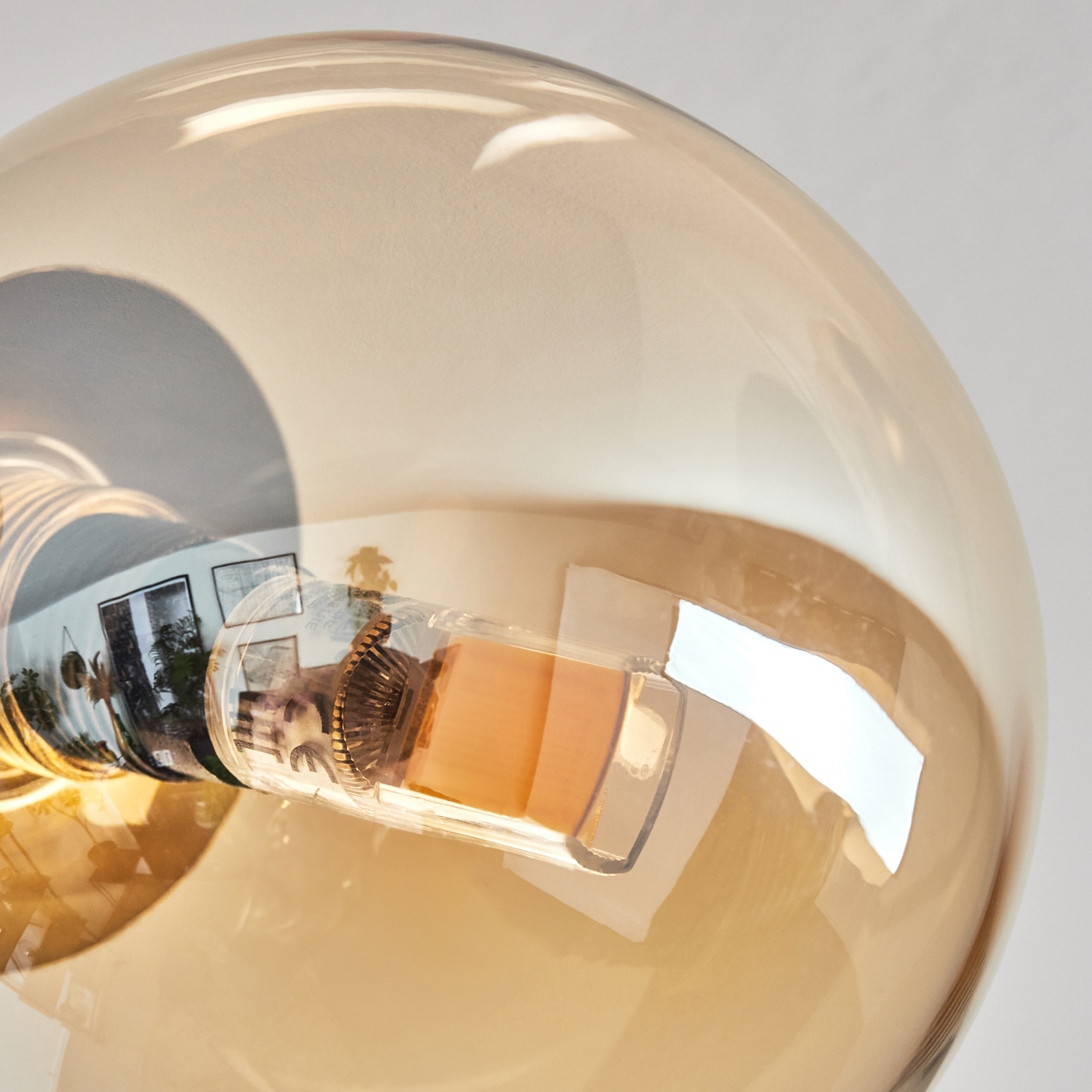 Nahaufnahme einer Glühbirne mit transparentem, bernsteinfarbenem Glas. Der Glühfaden ist sichtbar, Reflexionen zeigen Details eines Raumes.