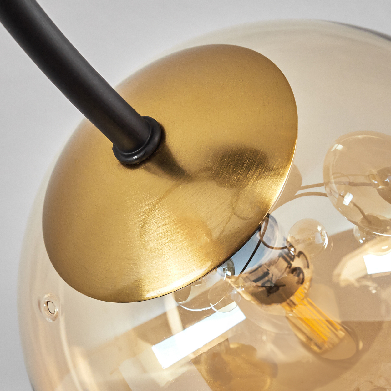 Nahaufnahme einer modernen Lampe. Sie hat eine Messingplatte, einen schwarzen Arm und eine transparente, bernsteinfarbene Glaskugel.