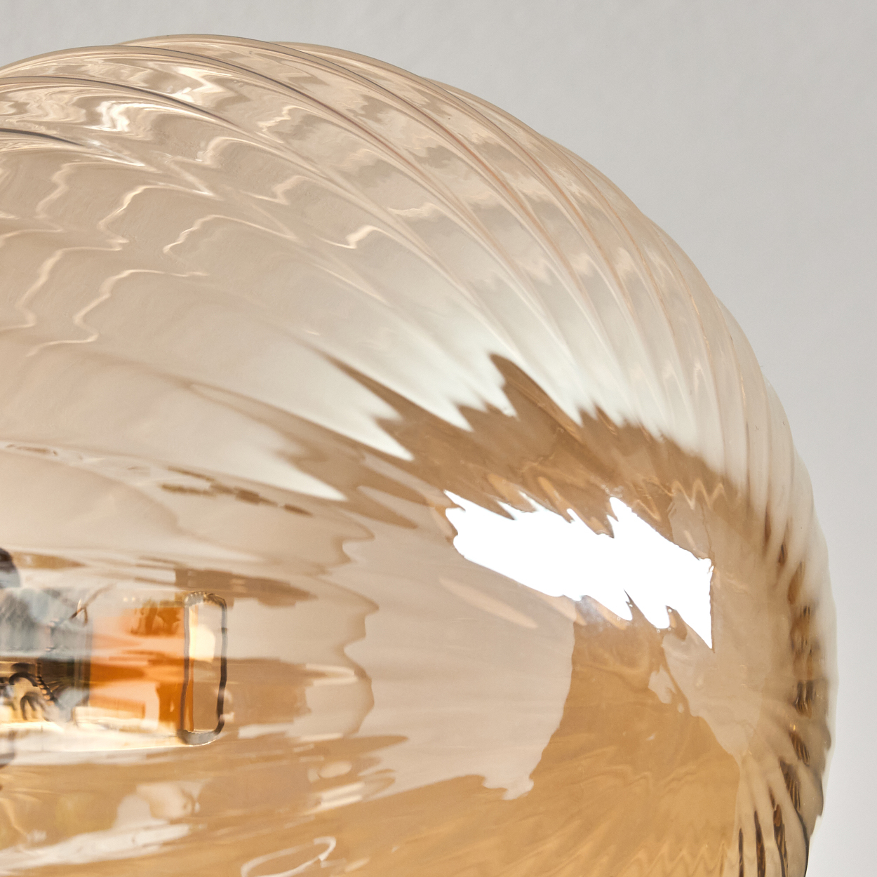 Nahaufnahme einer Leuchte. Der Glasschirm ist bernsteinfarben und hat ein Spiralmuster. Der Hintergrund ist weiß.