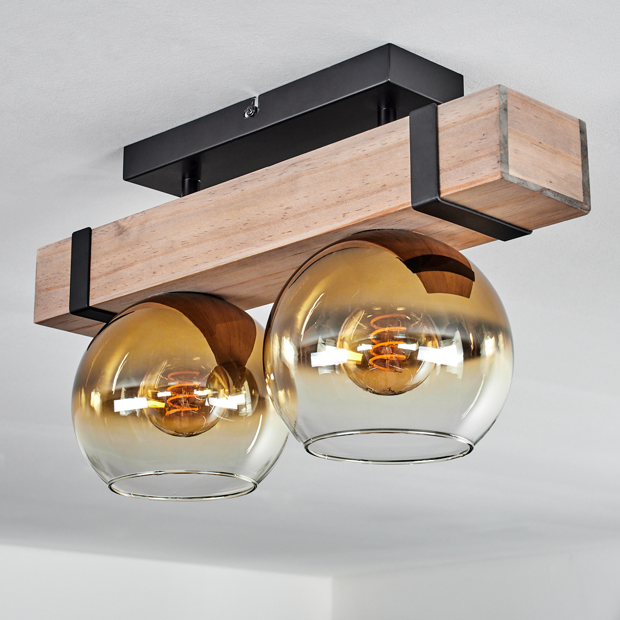 Eine Deckenleuchte mit zwei bernsteinfarbenen Glaskugeln, einem Holzbalken und einem schwarzen Metallrahmen. Die Glühbirnen sind sichtbar.