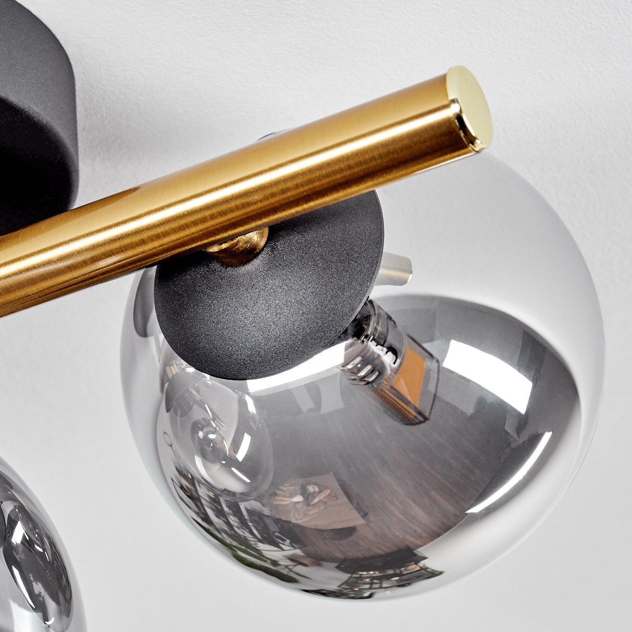 Nahaufnahme einer modernen Leuchte mit goldenem Metallstab, schwarzem Sockel und kugelförmigem Glasschirm. Der Hintergrund ist weiß.