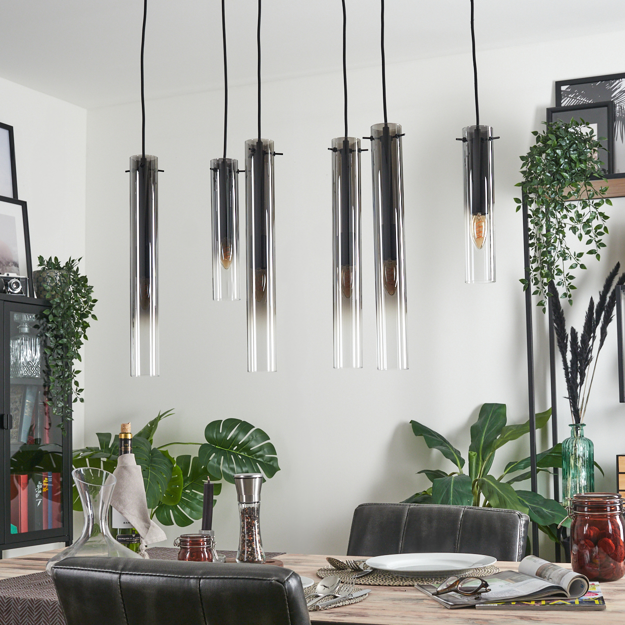 Esszimmer mit Hängelampen. Tisch mit Dekoration und Essen gedeckt. Grüne Pflanzen im Hintergrund. Schwarze Stühle im Vordergrund.