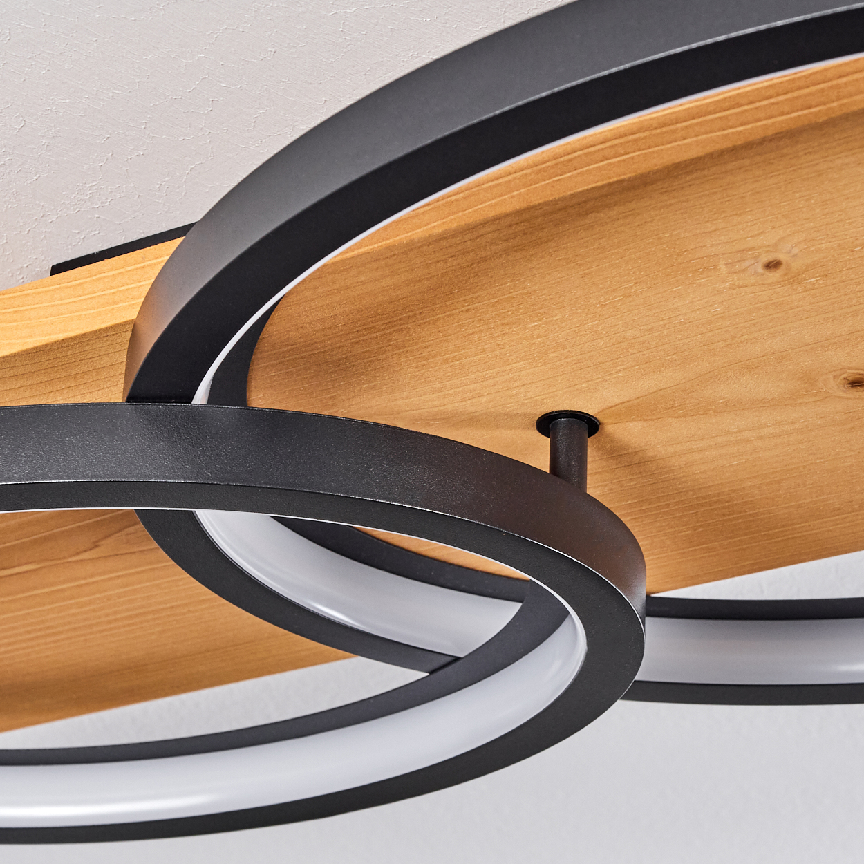 Moderne Deckenleuchte. Schwarze Metallringe mit weißen Lichtstreifen, montiert auf Holzplanken. Weißer Deckenhintergrund.