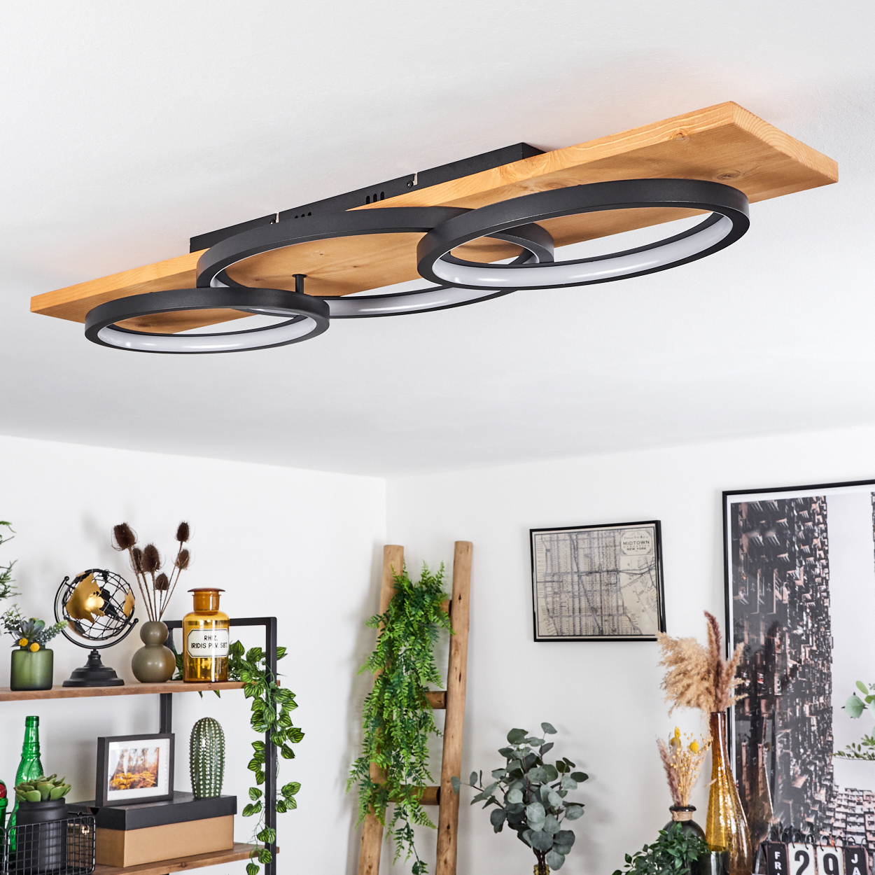 Deckenleuchte mit schwarzen Ringen und Holzbohlen. Regale mit Deko und Pflanzen darunter. Leiter und gerahmte Kunst an der Wand.