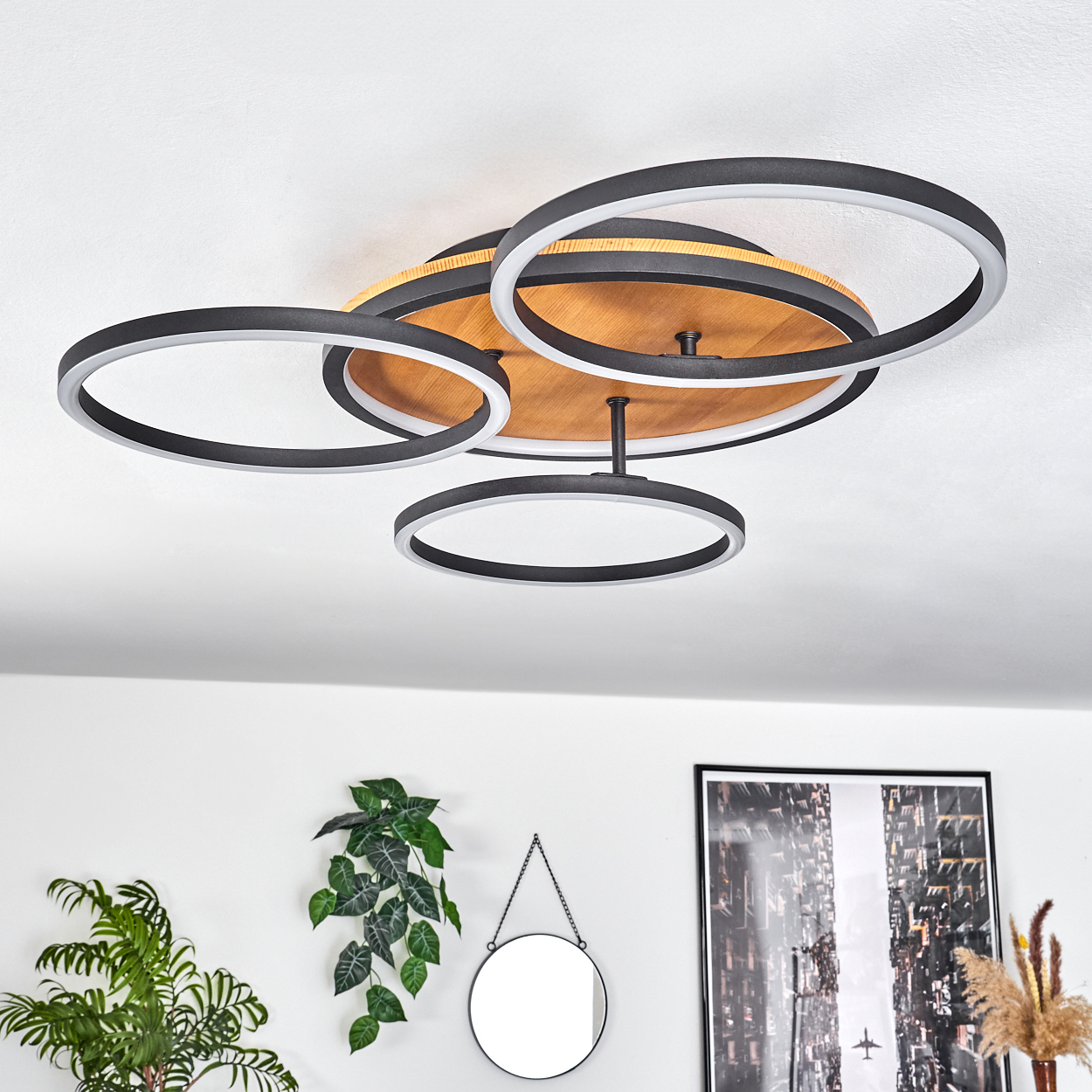 Moderne Deckenleuchte mit kreisförmigen schwarzen und weißen Ringen, Holzsockel und dekorativen Pflanzen und Spiegel im Hintergrund.