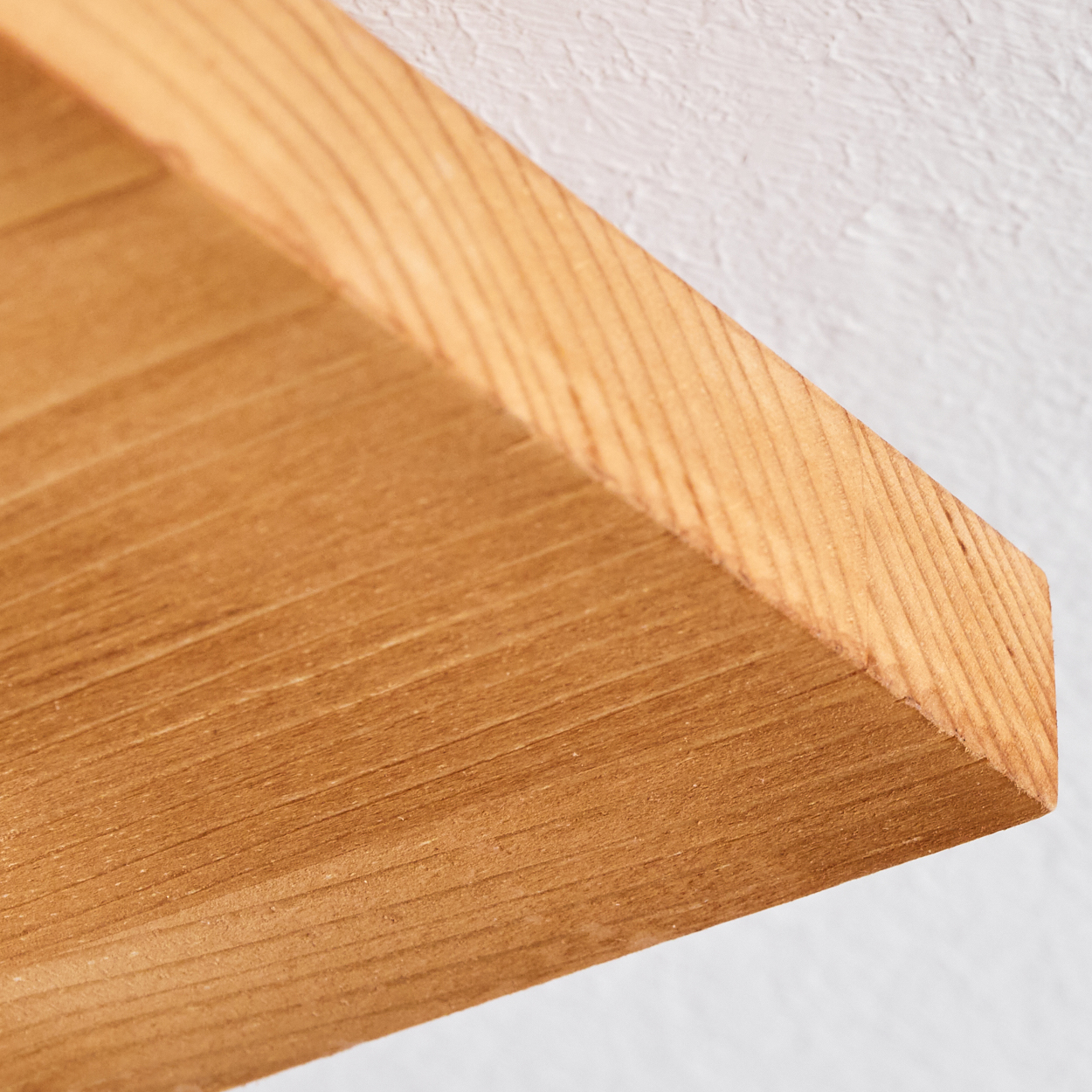 Nahaufnahme einer Holzeckablage vor einer weißen, strukturierten Wand. Das Holz ist hellbraun mit sichtbarer Maserung.