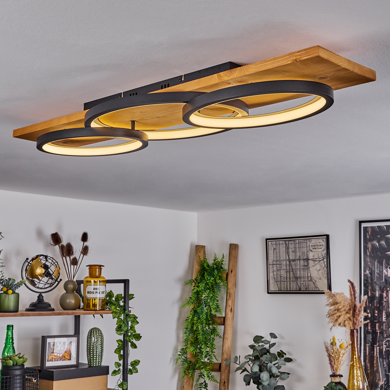 Eine moderne Deckenlampe mit drei kreisförmigen Lichtern. Die Holzbasis befindet sich über anderen Gegenständen auf dem Regal.