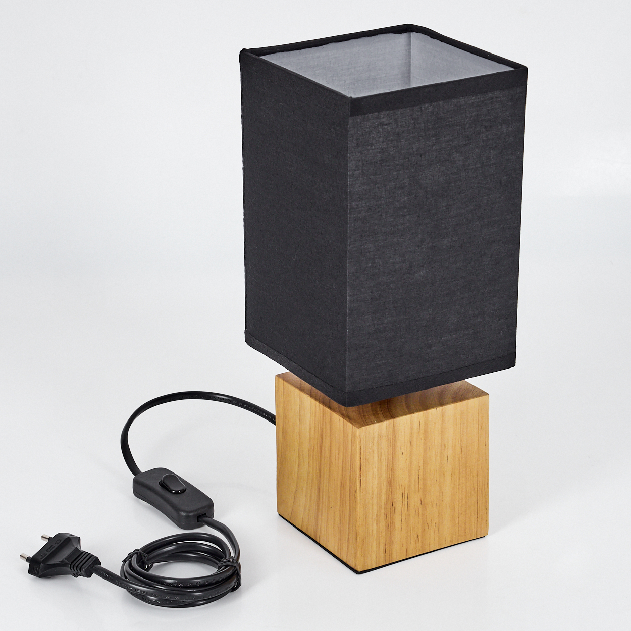 Ein schwarzer Lampenschirm sitzt auf einem Holzsockel. Ein Netzkabel mit Schalter und Stecker ist mit der Lampe verbunden, alles auf weißem Untergrund.