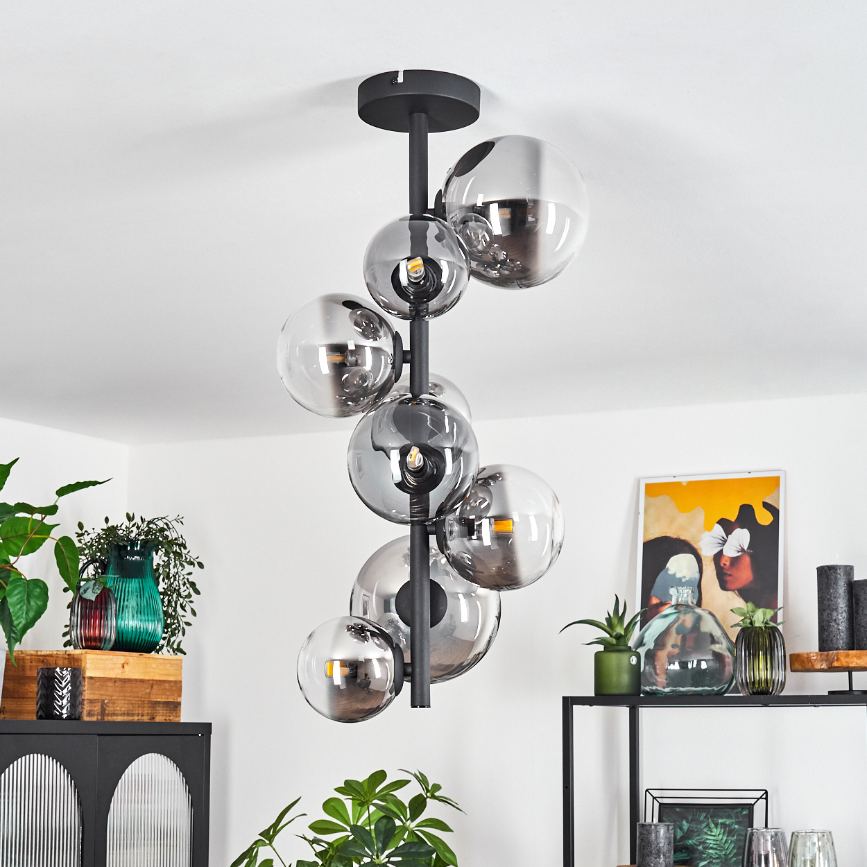 Eine moderne Deckenleuchte mit mehreren rauchfarbenen Glaskugeln hängt von der Decke. Der Raum hat Pflanzen und Dekorationsartikel.